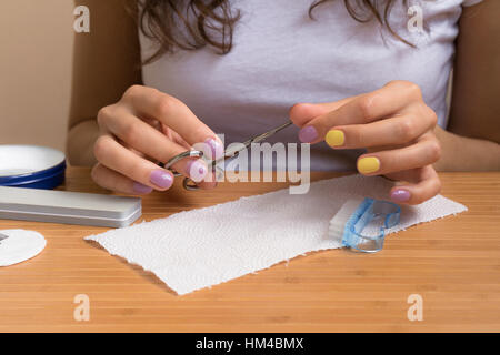 Weibliche Hände halten Nagelknipser. Ein junges Mädchen sitzt an einem Tisch und macht die Maniküre Scheren Closeup. Stockfoto