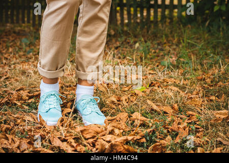 Weibliche Füße in Beige Hosen und ein Türkis Turnschuhe sind auf den abgefallenen Blättern. Herbst-Spaziergang. Stockfoto