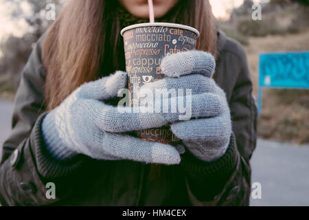 Junge Frau in Strickhandschuhe Kaffeetrinken aus Einweg-Becher mit einem Strohhalm im Herbst geht. Stockfoto