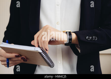 Frau in einem Geschäft passen, halten Sie ein Notebook und schaut auf ihre Uhr-Nahaufnahme Stockfoto