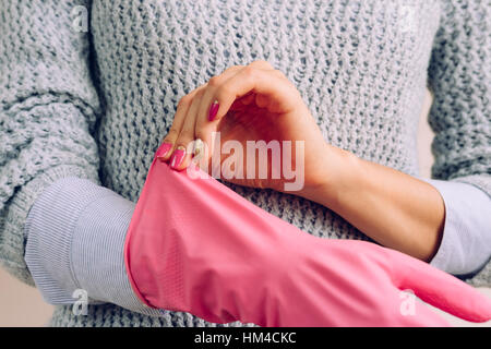 Frau in einem grauen Pullover und leuchtend rosa Maniküre trägt Gummihandschuhe für Hausreinigung Stockfoto