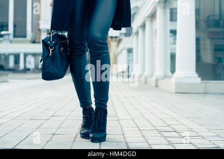 Details der Damenbekleidung. Nahaufnahme des weiblichen Beine in schwarzen Hosen und Stiefel. Frau zu Fuß in der Stadt, Low-Winkel zu schießen, kalten Tönen. Stockfoto