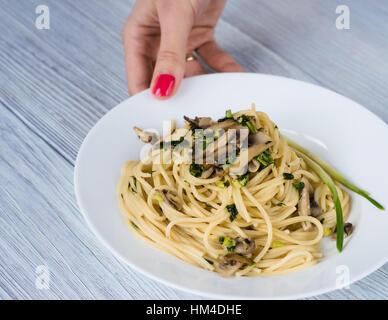 Weibliche Hand mit roten Maniküre weißen Halteplatte mit Nudeln und Pilzen Stockfoto