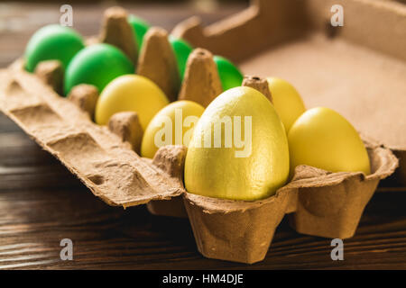 Offene Verpackung mit Hand bemalten Eiern. Gelbe und grüne Ostereier auf einem Holztisch. Stockfoto