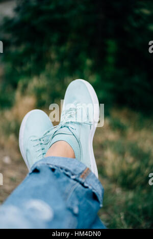 Nahaufnahme des weiblichen Beine in Jeans und Turnschuhen auf einem Hintergrund von Bäumen. Geringe Schärfentiefe, Textfreiraum. Stockfoto