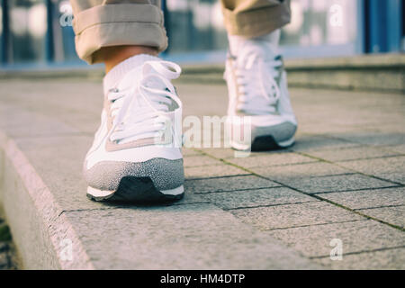 Weibliche Füße in weißen Turnschuhen, die zu Fuß auf dem Bürgersteig, niedrigen Winkel, Retro-Farben. Stockfoto