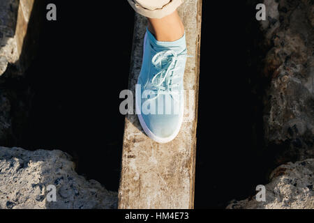 Weibliche Beine in Beige Hosen und Turnschuhe sind auf dem Brett über die Klippe Stockfoto