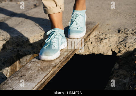 Weibliche Füße in Beige Hosen und Turnschuhe sind auf dem Board in den Abgrund Stockfoto