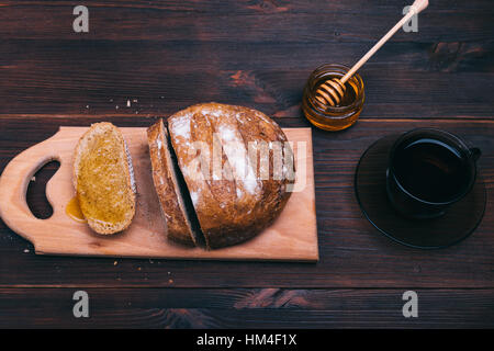 Schneiden von Brot, Honig und eine Tasse Tee in einer braunen Tischplatte Ansicht Stockfoto
