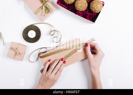 Weibliche Hände mit roten Maniküre packen die Geschenke in Schachteln und binden sie mit Bändern, Ansicht von oben Stockfoto
