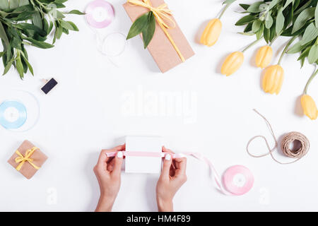 Weibliche Hand gebunden Band Box mit einem Geschenk auf weißen Tisch, Ansicht von oben Stockfoto