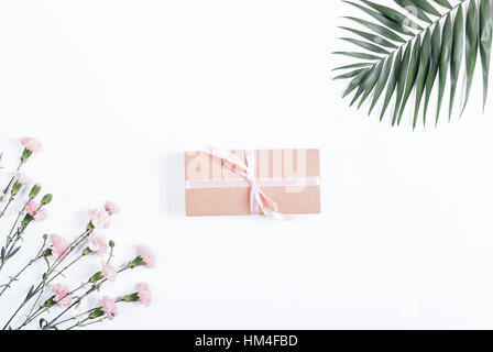 Box mit Band und Geschenk liegt auf einem weißen Tisch neben Blumen, Ansicht von oben Stockfoto