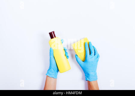 Weibliche Hände in blaue Gummihandschuhe mit einer gelben Flasche Reinigungsmittel und Schwamm, Ansicht von oben Stockfoto
