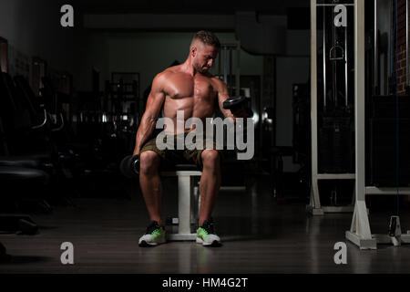 Gut aussehender Mann In einem dunklen Fitnessstudio - Kurzhantel Konzentrationscurls Bizeps trainieren Stockfoto