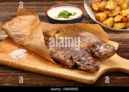 Gebackener Fisch eingewickelt in Papier mit Kartoffeln und weißen Dip auf hölzernen Hintergrund Stockfoto