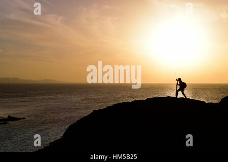 die Silhouette einer unkenntlich jungen Mannes eine Aufnahme direkt am Meer in der Dämmerung, gegen eine bunte orange sky Stockfoto