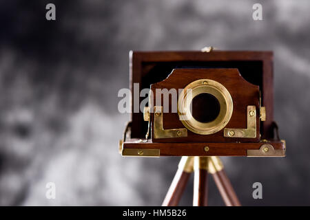eine alte hölzerne faltbare Kamera in einem Holzstativ, vor einem Farbverlauf grauen Hintergrund Stockfoto
