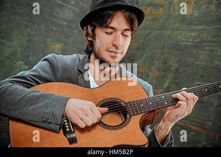 Cooler Typ mit Gitarre auf grauem Hintergrund Hut Stockfoto