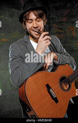 Cooler Typ mit Gitarre auf grauem Hintergrund Hut Stockfoto