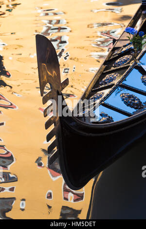 Gondel-Detail im goldenen Sonnenlicht mit dem Bau von Spiegelungen im Wasser an Venedig, Italien im Januar Stockfoto