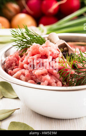 Rohes Hackfleisch in weiße Schüssel. Hackfleisch vom Schwein auf einem Hintergrund von frischem Bio-Gemüse Stockfoto