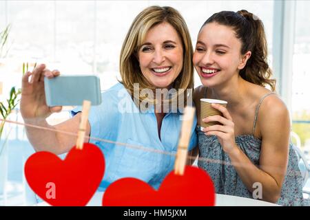 Frauen, die eine Selfie auf Handy gegen hängende Herzen rot Stockfoto