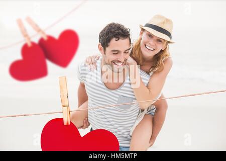 Zusammengesetztes Bild der roten hängenden Herzen und Mann Frau Huckepack verleihen Stockfoto