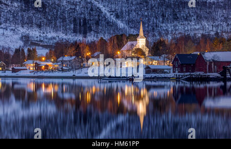 Abend in der kleinen Stadt Rognan in Nordnorwegen oberhalb des Polarkreises. Am Ufer des Fjords ist eine beleuchtete evangelische Kirche. Stockfoto