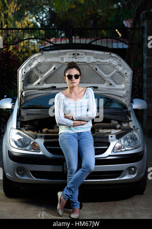 Mädchen mit verschränkten Armen mit offener Motorhaube des Autos Stockfoto