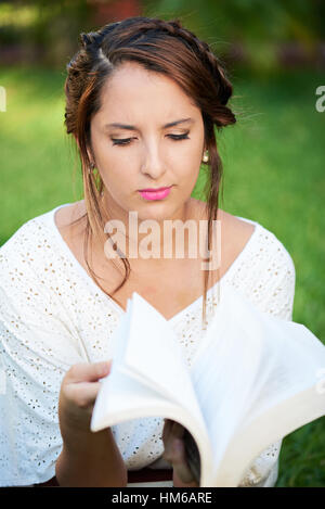 junge Frau Suche Buch über Grass park Stockfoto