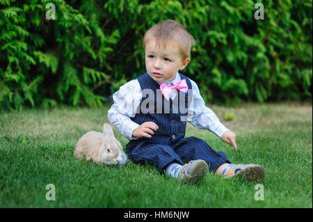 kleinen Jungen sitzen auf dem Rasen mit einem Kaninchen Stockfoto