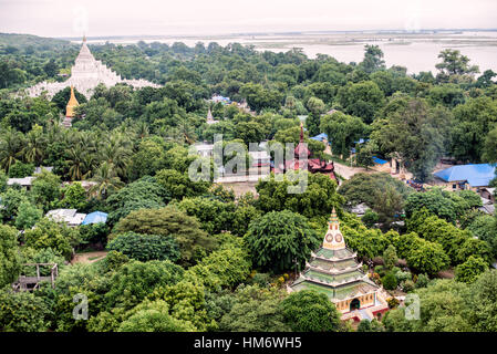 Hsinbyume-Pagode Mingun-Glocke Ayeyarwady-Fluss Luftaufnahme Myanmar | MINGUN, Myanmar — Vom Gipfel des Mingun Pahtodawgyi aus gesehen, erheben sich die weißen, stufenartigen Terrassen der Hsinbyume-Pagode links, während das rote Pavillon-Dach, das die Mingun-Glocke beherbergt, in der Mitte sitzt, beide eingerahmt vom Ayeyarwady-Fluss dahinter. Innerhalb einer einzigen Generation von Bodawpayas Herrschaft erbaut, bilden die drei Denkmäler einen Flusskomplex: der große Stupa, begonnen 1790, die Glocke, gegossen 1808, und Hsinbyume, vollendet 1816. Stockfoto