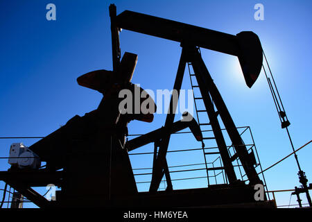 Ölfeld Bohrschwengels, rostig und alt, Silhouette durch die Sonne. Klarer blauer Himmelshintergrund. Zeigt Ölfeld Leben, Erdölindustrie und fossile Brennstoffe. Stockfoto