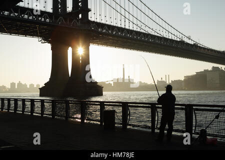 Mann Angeln von der East River Esplanade mit Blick auf die Brooklyn Waterfront unter die Manhattan Bridge Stockfoto