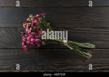 Blumenstrauß mit einem Band an der dunklen hölzernen Oberfläche trocken. Stockfoto