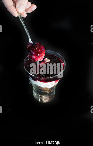 Käsekuchen im Glas mit Löffel isoliert in schwarz Stockfoto