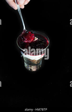 Käsekuchen im Glas mit Löffel isoliert in schwarz Stockfoto