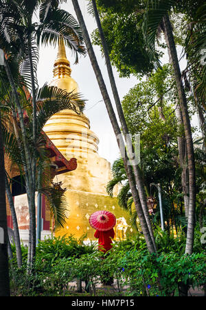 Frau Tourist mit roten traditionelle Thai Regenschirm in der Nähe von goldenen Stupa Tempel Wat Phra Singh in der Nähe von tropischen Bambusgarten in Chiang Mai, Thailand Stockfoto