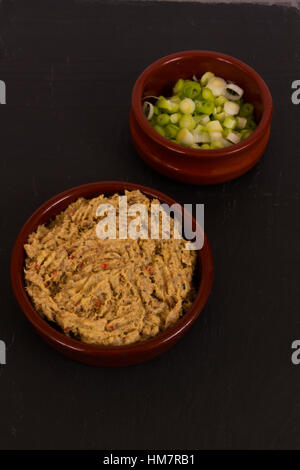 Hausgemachte geräucherte Makrele Pastete in einer Keramikscheibe serviert mit in Scheiben geschnittenen Frühlingszwiebeln auf Schiefer Hintergrund. Stockfoto