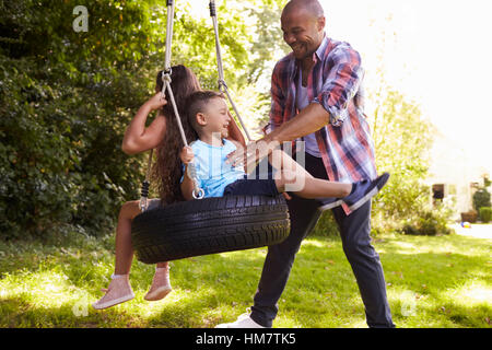 Vater drängen Kinder auf Reifenschaukel im Garten Stockfoto
