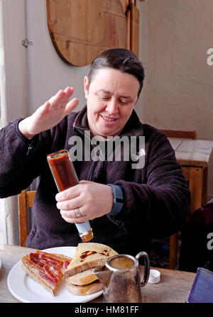 Applying Reife Frau Hähne HP Brown Sauce Flasche über ihr Frühstück Stockfoto