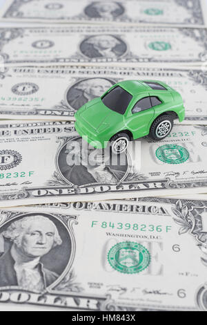 Kleine grüne Spielzeugauto auf uns 1 Dollar/1 $ Rechnungen. Als Metapher für die Kosten des Autofahrens und Benzin in den USA und die green fuel/grüne Wirtschaft. Stockfoto