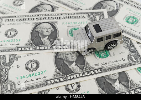 Kleine silberne Spielzeugauto auf uns 1 Dollar / 1 $ Rechnungen. Als Metapher für die Kosten für Autofahren und Benzin in den USA. Stockfoto