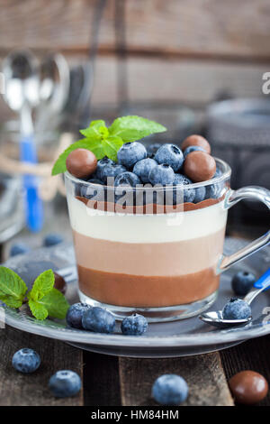 Köstliches Dessert der drei geschichteten Schokoladen-Mousse, dekoriert mit frischen Heidelbeeren, Minze und Bonbons, serviert im Glas-Tasse Stockfoto