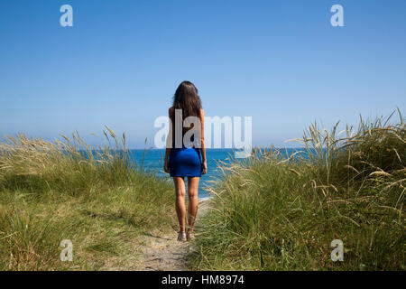 Hinten Ansicht Porträt der jungen Erwachsenen Frau Blick auf das Meer von Sanddüne mit hohen Gräsern Stockfoto