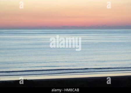 Die Sonne hat nur sank von Blick über dem Pazifischen Ozean und am Himmel leuchtet mit rosa, lila und orange Farbtöne als Brandung gegen das Ufer. Stockfoto