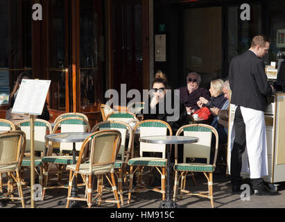 Frau sitzt vor einem Café in Paris im Winter Stockfoto