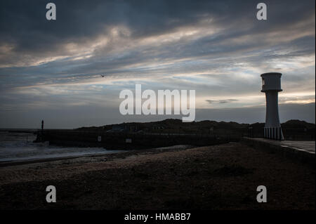 Ein Leuchtturm ist gegen den Himmel voller Wolken bei Sonnenuntergang am Strand in Littlehampton, West Sussex, UK Silhouette. Stockfoto