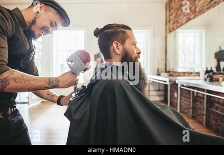 Bärtiger Mann ein Salon Cape im Barbershop, mit Friseur anpassen der Kopfstütze des Stuhls. Stockfoto