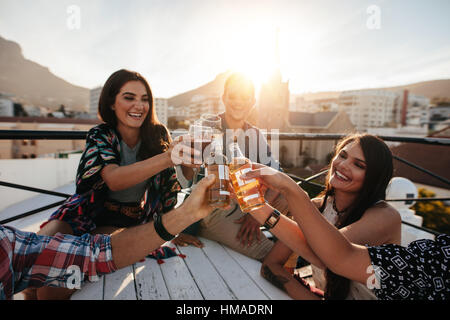 Glückliche junge Leute Toasten Getränke auf einer Party auf dem Dach. Jungen Freunden rumhängen und Getränke zu genießen. Stockfoto